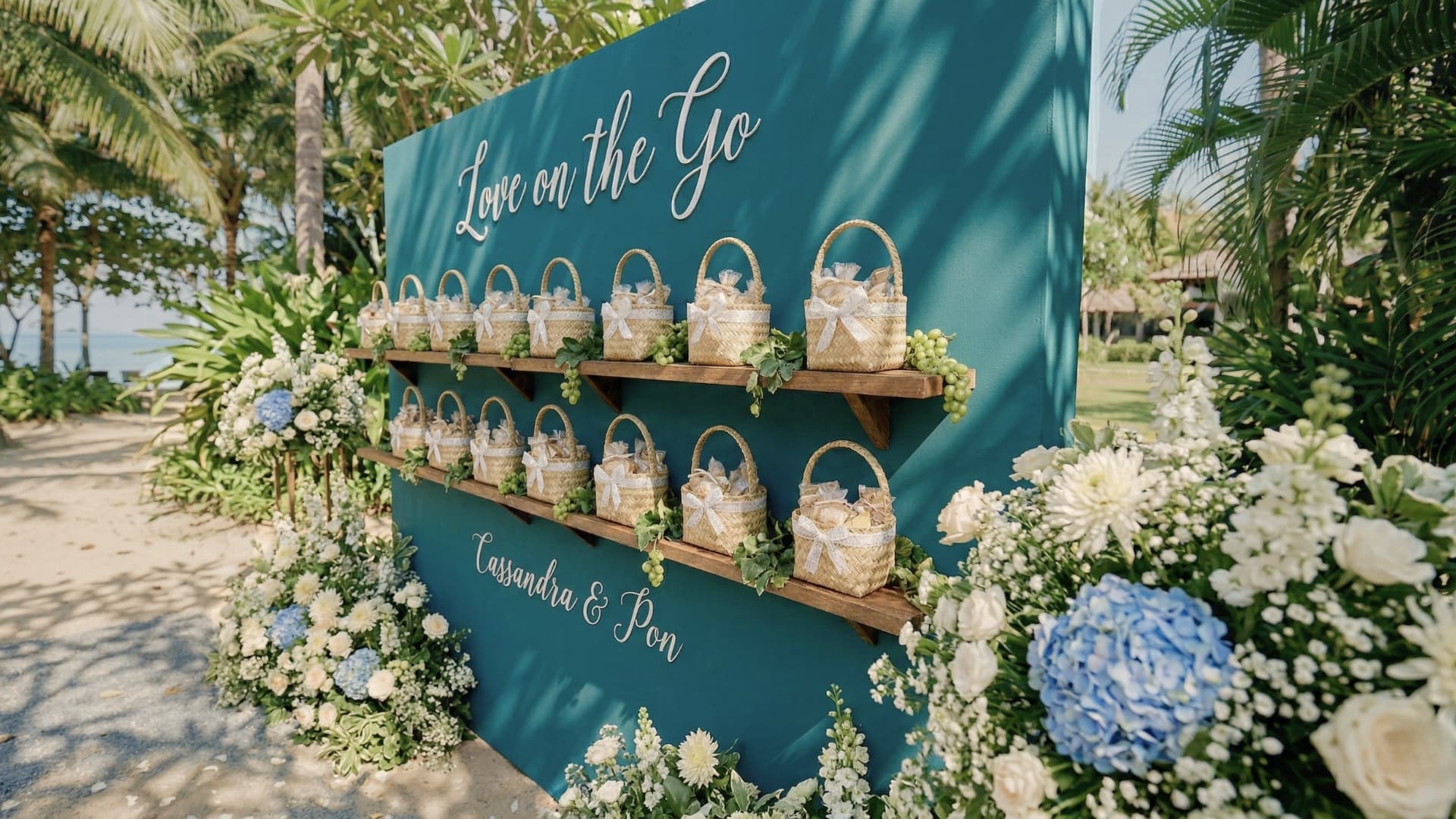 Beach wedding favor wall display framed by lush florals